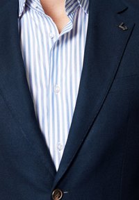 Granatowa marynarka z teksturowanej tkaniny, zapinana na jeden guzik, w połączeniu z jasnoniebieską koszulą w białe paski, z okrągłymi guzikami i kołnierzem typu spread.