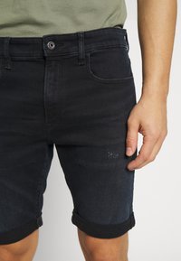 Svarta denimshorts med uppvikta nederkanter, med fem fickor, bältehällor och en metallknapp för stängning i midjan.