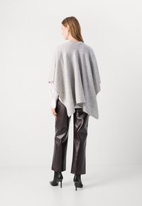 Grå uld poncho, løs pasform, rund halsudskæring. Matchet med skinnende burgunder kunstlæderbukser og sorte ankelstøvler. Minimalistisk design.