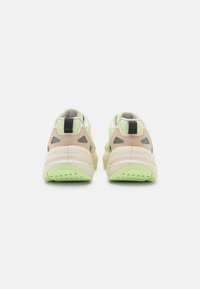 Beige Sportscchuhe mit einem strukturierten Obermaterial und einer neongrünen Außensohle. Zu den Merkmalen gehören ein gepolsterter Kragen und ein schwarzer Akzent an der Ferse.