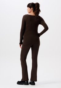 Brauner Langarm-Oberteil und passende ausgestellt geschnittene Hose aus weichem Material, mit Rundhalsausschnitt und figurbetonter Silhouette. Schwarze Plateauschuhe.