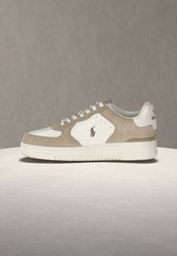 Pantof sport tip low-top din piele întoarsă bej și piele albă, cu șireturi albe și un logo mic și închis la culoare pe panoul lateral.