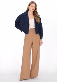 Marineblauwe cropped jas met dubbele rij knopen, gecombineerd met beige wijde broek met hoge taille, voorzien van een ceintuur en zachte stof.