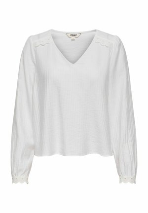 Bijela bluza s dugim rukavima i V-izrezom, teksturiranog tkanja, s nazubljenim rubovima i detaljima s izrezima na ramenima i manžetama.