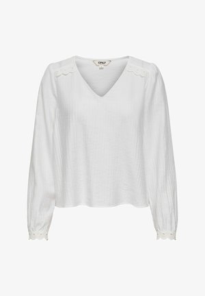 Bijela bluza s dugim rukavima i V-izrezom, teksturiranog tkanja, s nazubljenim rubovima i detaljima s izrezima na ramenima i manžetama.