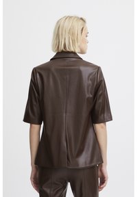 Veste en cuir marron à manches courtes avec un col structuré et une coupe ajustée. Texture lisse avec des détails de couture au dos.