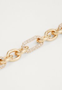 Gullkjede armbånd med vekslende glatte og teksturerte lenker, prydet med klare krystaller i oval innfatning.