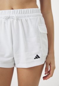 Beli bombažni kratki hlače z elastičnim pasom, podrobnostjo s šnurico, stransko žepom in črnim Adidasovim logotipom na spodnjem robu.