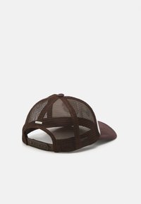 Brown mesh trucker cap with a curved visor, adjustable snapback closure, and a small metal logo accent on the left side.