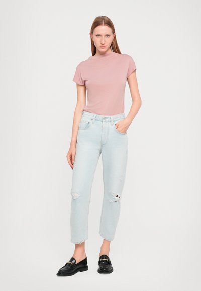 T-shirt rosa a maniche corte abbinata a jeans chiari strappati. Il modello indossa mocassini neri. Design semplice e moderno con una vestibilità rilassata.