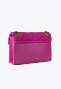 Paarse quilted suède handtas met een gladleren bodem. Voorzien van goudkleurige hardware en een logo dat op de voorkant is geperst. Compacte rechthoekige vorm.