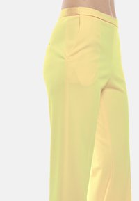 Pantaloni gialli a gamba larga realizzati in un tessuto leggero e morbido, dotati di tasche laterali e una vita senza cuciture per un aspetto curato.