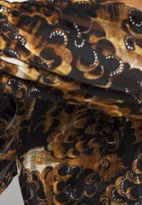 Tištěná blůza s abstraktním vzorem v černé, hnědé a béžové barvě, s jemnou texturou, plisovaným designem a knoflíkovými detaily na přední straně.