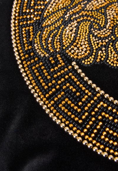 Μαύρο ύφασμα διακοσμημένο με περίτεχνα χρυσά και μαύρα καρφιά που σχηματίζουν κυκλικό μοτίβο, περιλαμβάνοντας γεωμετρικό περίγραμμα με μεταλλικές λεπτομέρειες.