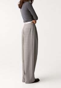 Haut gris à manches longues associé à un pantalon à carreaux taille haute, jambes larges, avec un motif à carreaux subtil et un détail de poche arrière.