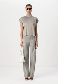 Top corto grigio chiaro a maniche corte con colletto alto, abbinato a pantaloni grigi chiaro a gamba larga. Gli accessori includono occhiali da sole neri e una borsa bianca.