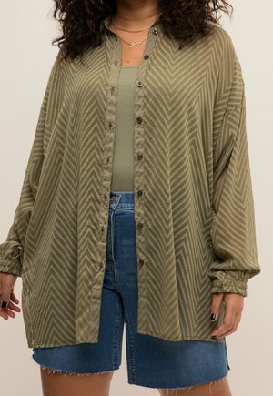 Personne portant une chemise boutonnée à motif vert olive sur un débardeur assorti et un short en jean bleu avec un ourlet effiloché.