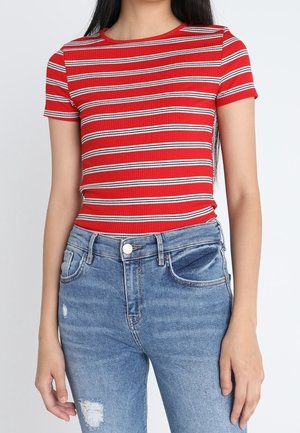 Haut à manches courtes rouge côtelé avec des rayures horizontales blanches et navy. Associé à un jean taille haute déchiré bleu clair.