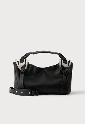 Borsa nera con dettagli di fibbie argento, manico corto e tracolla staccabile posta su una superficie bianca.