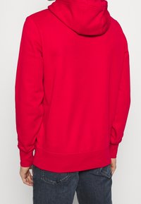 Rode hoodie van zachte stof, met een trekkoordkap, lange mouwen en een geribde onderrand. Gladde textuur zonder zichtbare patronen of accenten.