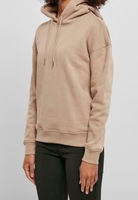 Sudadera con capucha color caqui con cordones, puños y bajo acanalados. Tela suave, corte relajado y sin patrones ni gráficos visibles.