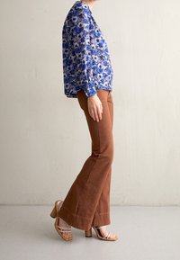 Blouse fleurie bleue à manches longues, assortie à un pantalon évasé en velours côtelé marron et des sandales à talons beiges à brides. Design simple et texturé.