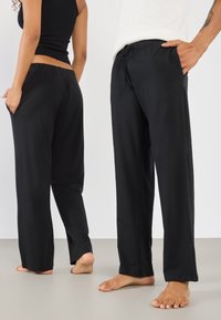 Pantalons noirs à cordon de serrage en tissu doux et respirant. Jambes droites et taille élastique. Comprend des poches latérales et une coupe décontractée.