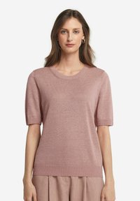 Ljusrosa kortärmad tröja i stickad tyg. Den har en rund halsringning och en ribbad fåll, med en slät textur och en figurnära siluett.