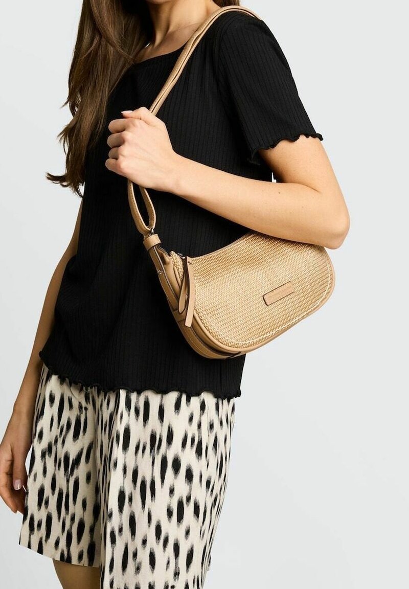 Femme portant un haut noir à manches courtes et un short imprimé léopard, tenant un sac à bandoulière beige tissé avec une fermeture éclair.
