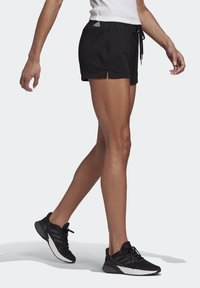 Svarta idrottsshorts med sidspringor och elastisk midja. Kombinerat med svarta sneakers med kontrasterande vita sulor och snördesign.