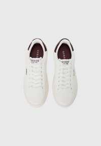 Sneaker bianca realizzata in pelle liscia con un tallone bordeaux testurizzato. Presenta lacci bianchi e un piccolo logo metallico sul lato.