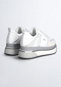 Baskets blanches avec des accents gris, dotées d'une semelle plateforme épaisse, de détails métalliques et d'un panneau latéral texturé. Marque apposée sur le talon.