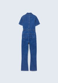Combinaison courte en denim bleu à manches courtes avec poches arrière et passants de ceinture, affichée à plat sur un fond clair uni.