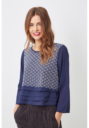 Blusa navy con un patrón geométrico bordado en la sección superior, con tres pliegues en el dobladillo y mangas largas.