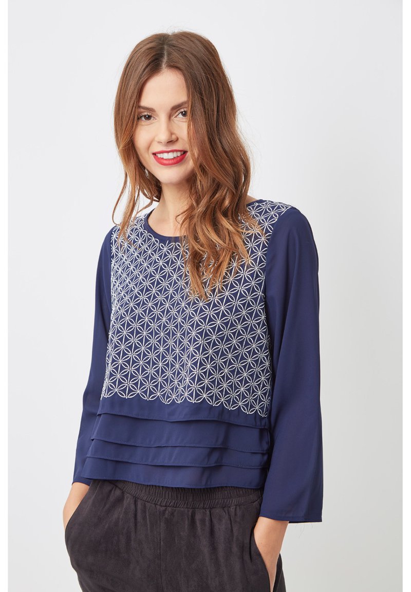 Blusa navy con un patrón geométrico bordado en la sección superior, con tres pliegues en el dobladillo y mangas largas.