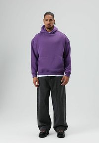 Hoodie violet avec une poche avant, associé à un jean gris foncé à jambes larges et des chaussures noires à plateforme. Style décontracté, coupe et design relax.