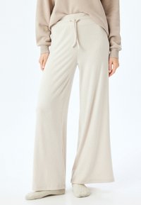 Pantalones de pierna ancha en beige claro, confeccionados con una tela texturizada, que cuentan con una cinturilla elástica con cordón para un ajuste ajustable.