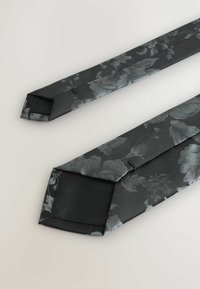 Czarny krawat w kwiatowy wzór, charakteryzujący się błyszczącą teksturą i eleganckim krojem z ostrymi końcami. Wykonany z gładkiego materiału przypominającego jedwab.