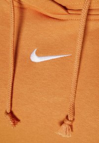 Orange sweatshirt med en strukturerad finish, med en vit Nike-logotyp och dragsko detaljer vid huvan. Mjuk, avslappnad design.
