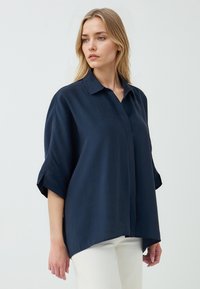 Marineblauwe oversized shirt met korte mouwen, een klassieke kraag en een losse pasvorm. Glad oppervlak met zijsplitten en een rechte zoom.