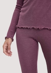 Geribbelde loungewear set in diep mauve, bestaande uit een longsleeve top met een gerimpelde zoom en bijpassende aansluitende broeken, die textuur en comfort benadrukken.