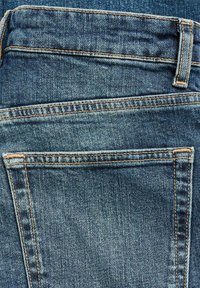 Blå denimjeans med en urtvättad struktur, med bakfickor som är omgivna av kontrasterande sömmar och en subtil tvätteffekt.