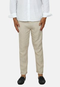 Pantaloni in lino beige con una vestibilità slim, caratterizzati da una texture liscia e orli arrotolati, abbinati a scarpe nere senza lacci.