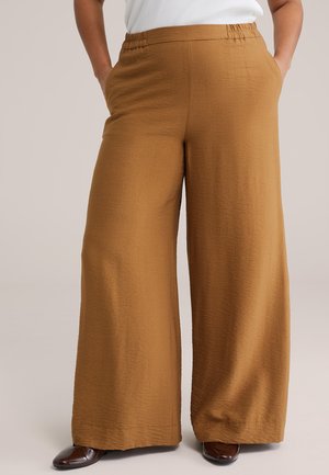 Široké hnedé nohavice s elastickým pásom a bočnými vreckami, nosené s hnedými topánkami a bielym topom, zobrazené od pása po nohy.