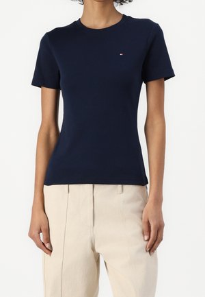 Granatowy bawełniany t-shirt z okrągłym dekoltem i krótkimi rękawami. Na piersi znajduje się małe logo. Uzupełniony jasnobeżowymi spodniami.