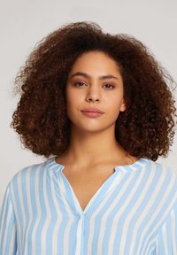 Blusa a rayas azul claro y blanca con cuello y cierre de botón, que presenta una tela suave y texturizada y un corte relajado.
