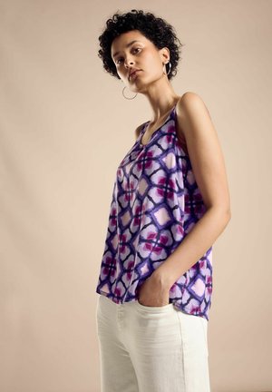 Lila gemusterte ärmellose Bluse mit geometrischen Formen und weicher Textur, kombiniert mit hellen Hosen. Verfügt über Seitentaschen.