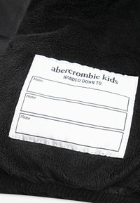 Must mustaimega pehme tekstuuriga must fliiskangas. Sisaldab valget silt, kuhu on kirjutatud nimed, millel on tikandiga äär ja bränd "abercrombie kids".