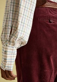 Langärmliges, karierter Hemd in Weiß-, Blau- und Brauntönen. Kombiniert mit kastanienbraunen Cordhosen mit gerippter Textur und Knopfdetails.