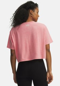 Camiseta rosa recortada hecha de tela suave, con mangas cortas y un logo en la parte trasera. Textura lisa, diseño casual.